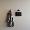 Beige Wand mit zwei schwarzen Haken, an einem hängt ein grauer Mantel, am anderen eine schwarze Tasche in schlichtem Stil