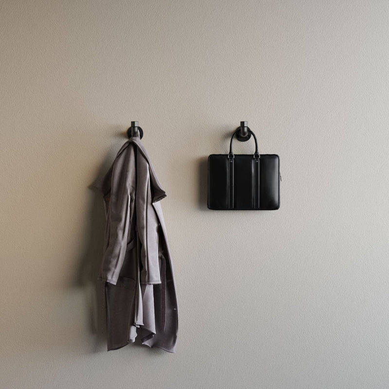 Beige Wand mit zwei schwarzen Haken, an einem hängt ein grauer Mantel, am anderen eine schwarze Tasche in schlichtem Stil